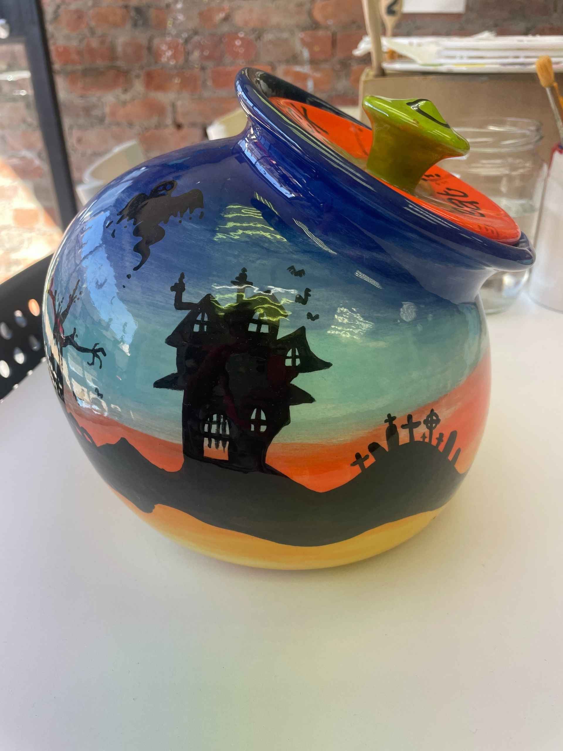 A Halloween-themed ceramic pot featuring a spooky house design, perfect for seasonal decorations.