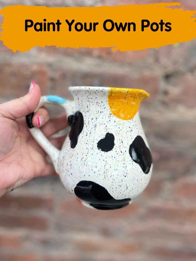A traditional cow print mug adorned with extra splashes of orange and blue paint. Pot painting in Hillsborough