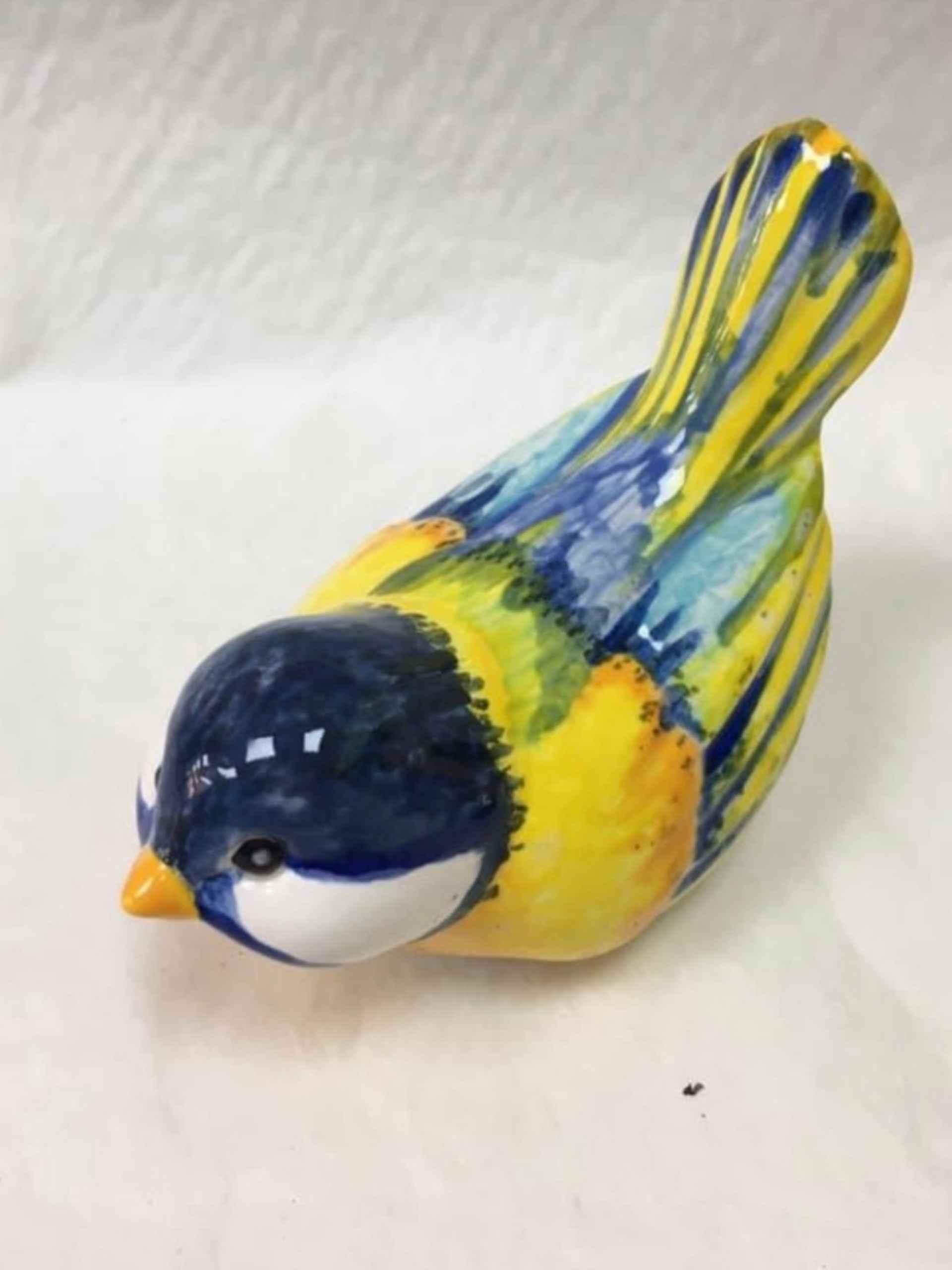 A ceramic bird made in a pottery studio, featuring a vibrant yellow and blue head, showcasing intricate craftsmanship and artistic design.