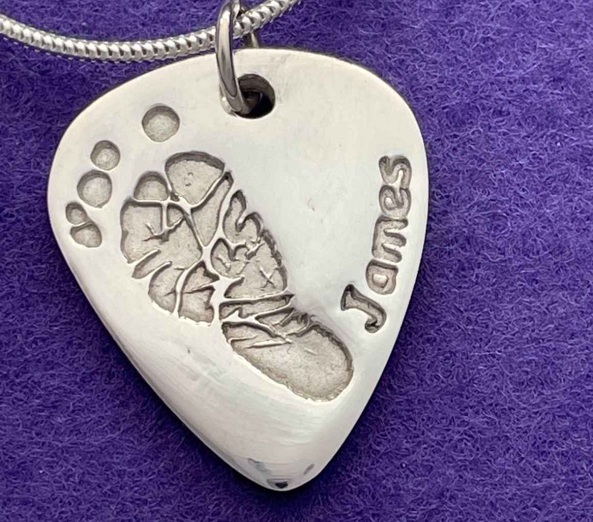 A silver pendant featuring a unique footprint design etched onto its surface. The perfect place for crafts in Hillsborough