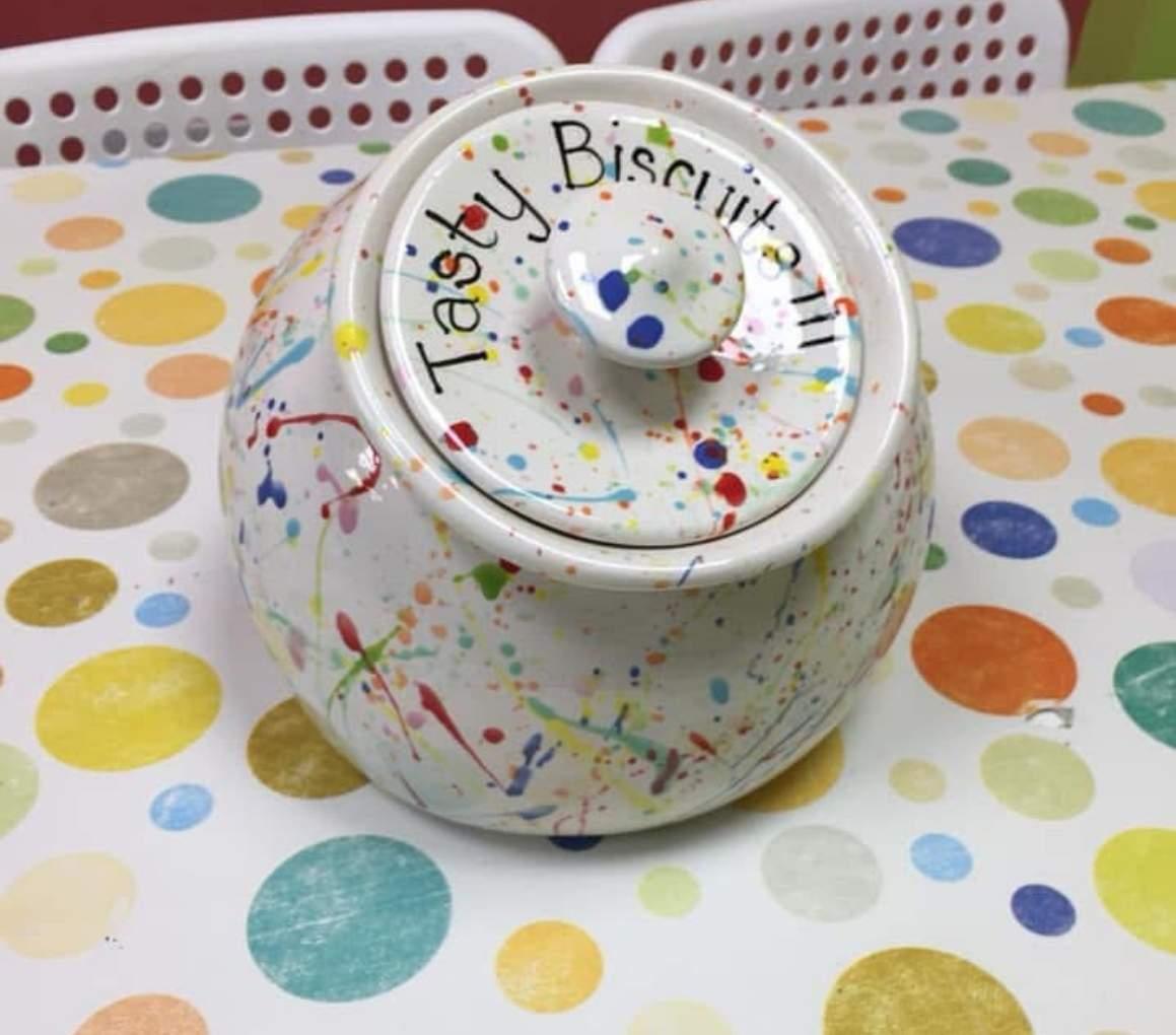 A white ceramic jar adorned with colourful paint splatters, showcasing an artistic and vibrant design.